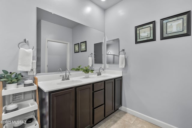 full bath featuring tile patterned flooring, double vanity, baseboards, and a sink