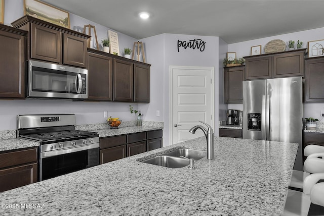 kitchen with light stone countertops, dark brown cabinetry, a kitchen breakfast bar, stainless steel appliances, and a sink