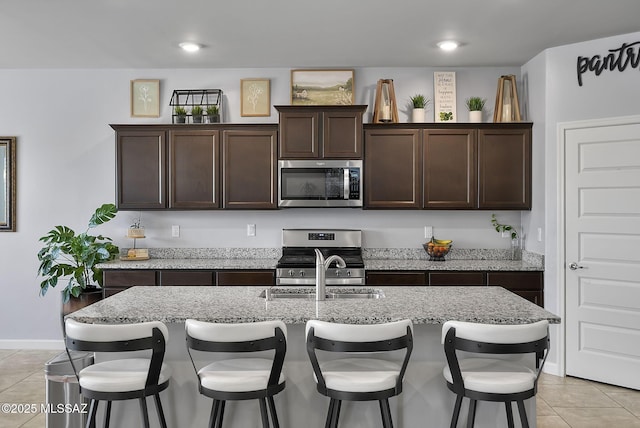 kitchen with dark brown cabinetry, a kitchen bar, appliances with stainless steel finishes, light tile patterned flooring, and a sink