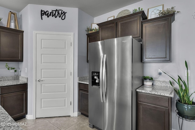 kitchen with light tile patterned floors, light stone countertops, dark brown cabinets, and stainless steel fridge with ice dispenser