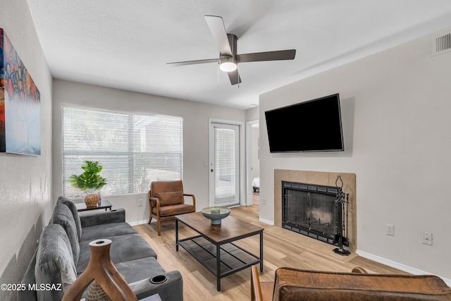 living room with a ceiling fan, a fireplace, light wood-type flooring, and baseboards