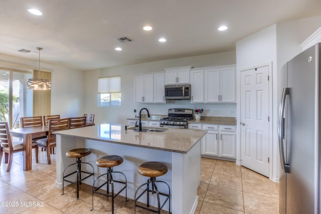 kitchen featuring light stone counters, visible vents, a sink, appliances with stainless steel finishes, and white cabinetry