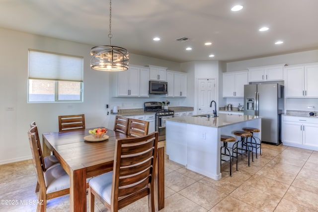 kitchen with a sink, a chandelier, appliances with stainless steel finishes, white cabinets, and a kitchen island with sink