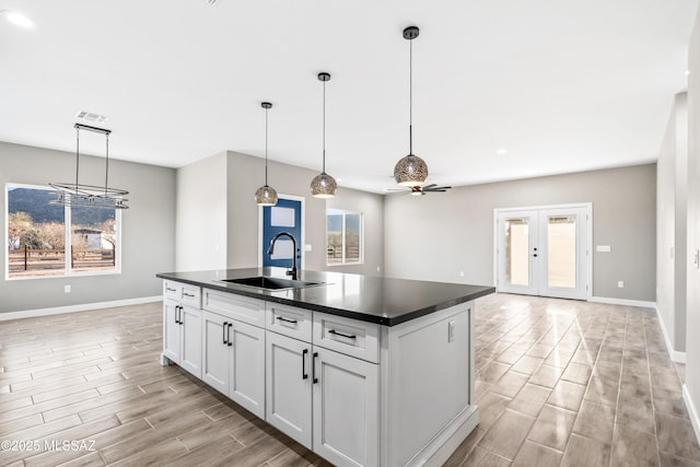 kitchen with dark countertops, wood finish floors, a center island with sink, white cabinetry, and a sink