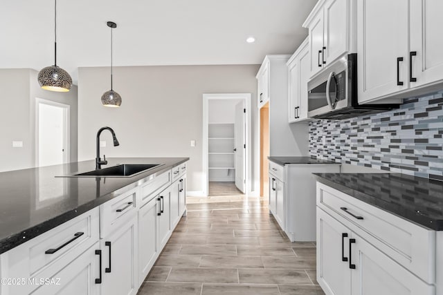 kitchen featuring stainless steel microwave, backsplash, dark stone counters, white cabinets, and a sink