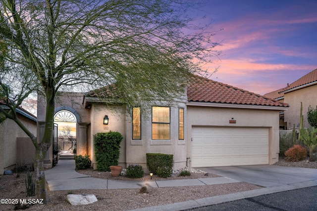 mediterranean / spanish house with stucco siding, a garage, driveway, and a tile roof