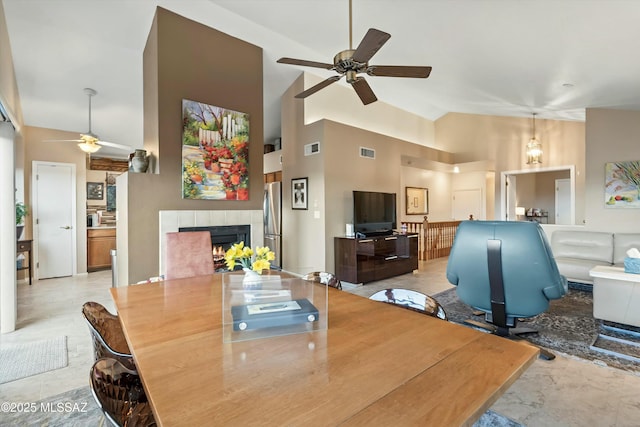 dining space featuring visible vents, a tile fireplace, high vaulted ceiling, and ceiling fan