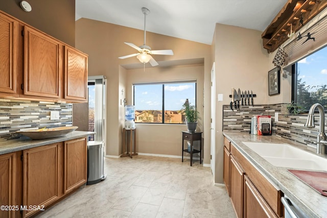 kitchen featuring a ceiling fan, brown cabinetry, lofted ceiling, a sink, and stainless steel dishwasher