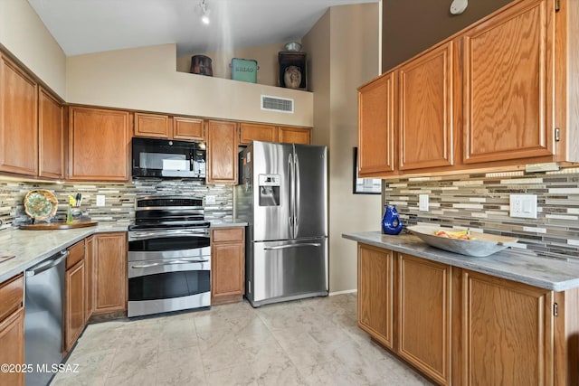 kitchen with visible vents, backsplash, vaulted ceiling, brown cabinets, and appliances with stainless steel finishes