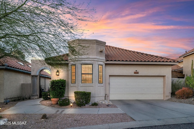 mediterranean / spanish-style home featuring stucco siding, a garage, concrete driveway, and a tiled roof