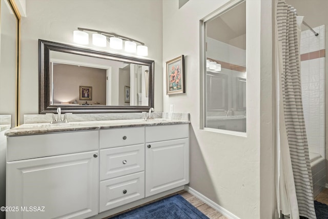 bathroom featuring a tile shower, a sink, wood finished floors, and double vanity