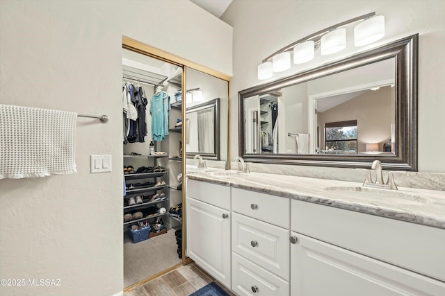 full bathroom with a sink, a walk in closet, double vanity, and vaulted ceiling