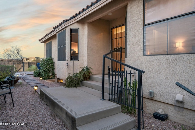 entrance to property with a gate, stucco siding, a tile roof, and fence