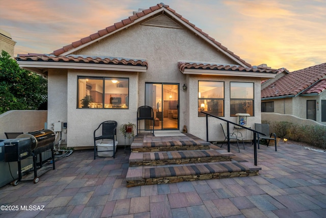 back of house at dusk featuring stucco siding, a tile roof, and a patio area