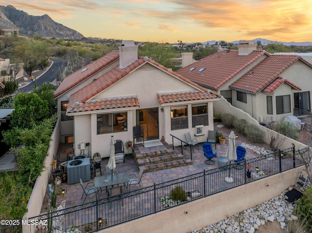 back of house at dusk with a patio area, a mountain view, a tiled roof, and central air condition unit