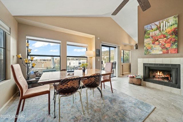 dining space with baseboards, high vaulted ceiling, and a tile fireplace