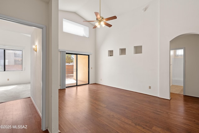 empty room featuring hardwood / wood-style floors, a ceiling fan, arched walkways, and high vaulted ceiling