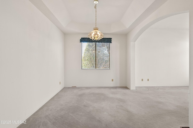 spare room with a tray ceiling, arched walkways, carpet floors, and a chandelier