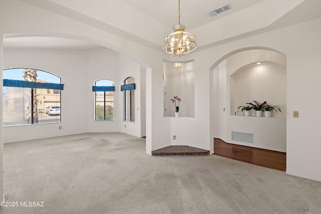 spare room featuring a tray ceiling, visible vents, carpet, and a chandelier