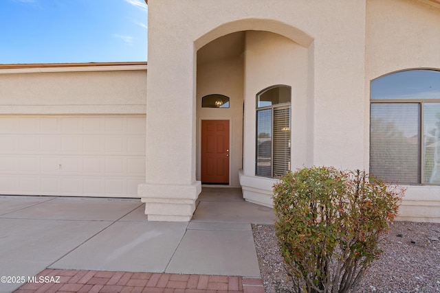 doorway to property with stucco siding, a garage, and concrete driveway