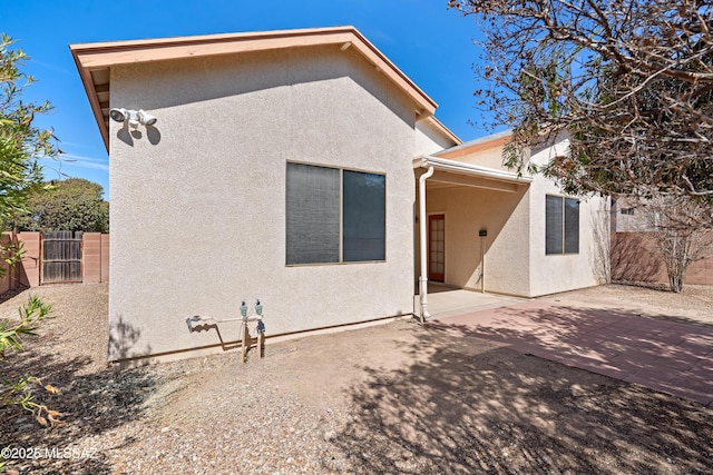 rear view of property featuring a gate, stucco siding, a patio, and fence