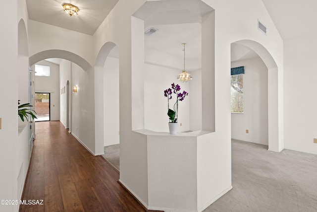 hall with wood finished floors, visible vents, a towering ceiling, and arched walkways