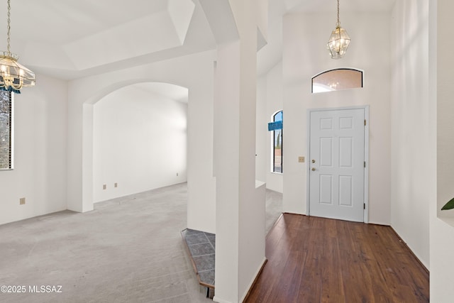 foyer entrance featuring carpet, wood finished floors, a towering ceiling, a raised ceiling, and a notable chandelier