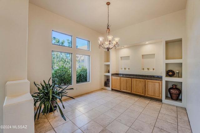 kitchen featuring dark stone countertops, built in shelves, light tile patterned floors, an inviting chandelier, and decorative light fixtures