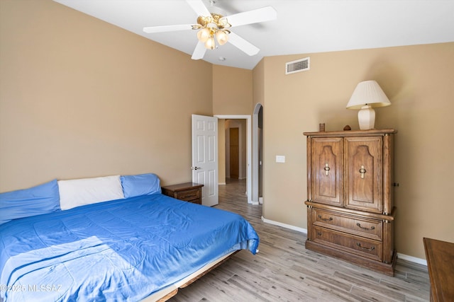 bedroom with visible vents, arched walkways, lofted ceiling, and light wood finished floors