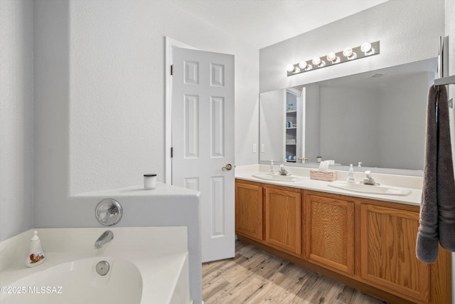 full bathroom featuring double vanity, wood finished floors, a garden tub, and a sink