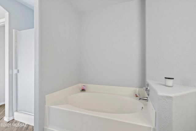 bathroom featuring a stall shower, wood finished floors, and a bath