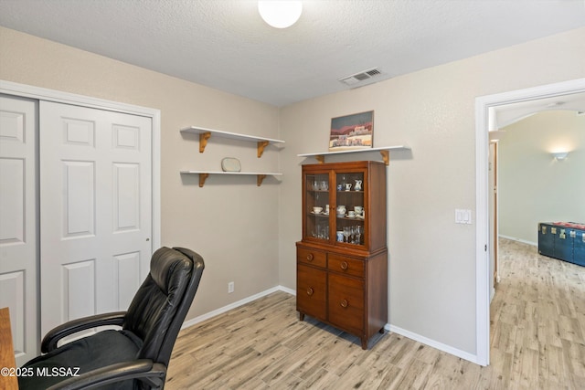 home office featuring a textured ceiling, baseboards, visible vents, and light wood-type flooring