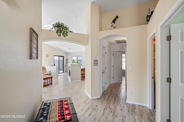 hall with visible vents, baseboards, lofted ceiling, arched walkways, and light wood-style floors