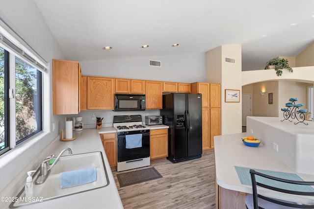 kitchen featuring black appliances, vaulted ceiling, visible vents, and a sink