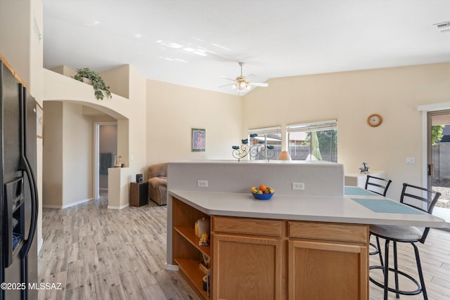 kitchen featuring a kitchen bar, black fridge, arched walkways, light wood-style floors, and light countertops