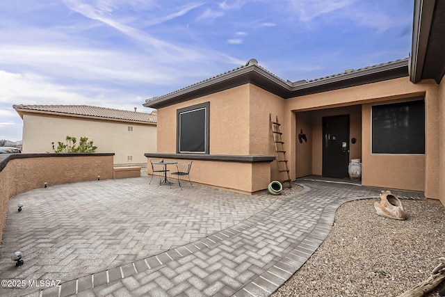 doorway to property featuring a tiled roof, a patio area, and stucco siding