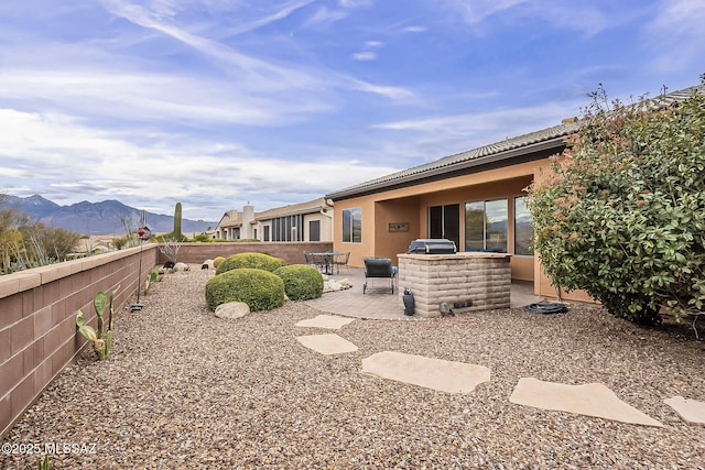 back of property with stucco siding, fence, a mountain view, exterior kitchen, and a patio area