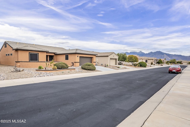 view of front of house featuring stucco siding, driveway, a tile roof, a mountain view, and a garage