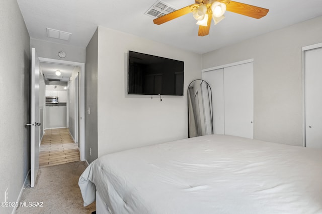 bedroom with visible vents, multiple closets, ceiling fan, attic access, and carpet flooring