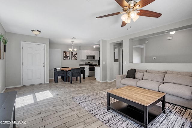 living room with ceiling fan with notable chandelier, baseboards, and light wood-style floors