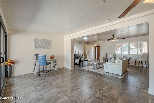 living room featuring baseboards, a textured ceiling, and ceiling fan