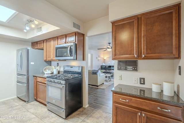 kitchen featuring visible vents, dark stone countertops, brown cabinets, stainless steel appliances, and a ceiling fan