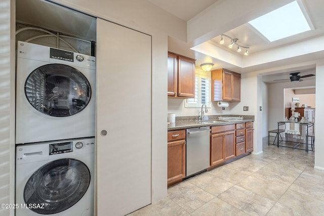 interior space featuring brown cabinets, a sink, a tray ceiling, stacked washer / drying machine, and dishwasher