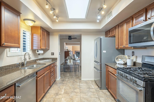 kitchen with dark stone counters, a tray ceiling, appliances with stainless steel finishes, and a sink