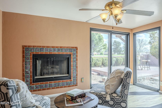 living room with a tile fireplace, baseboards, ceiling fan, and wood finished floors