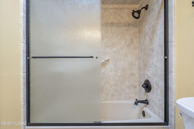 bathroom with toilet and bath / shower combo with glass door