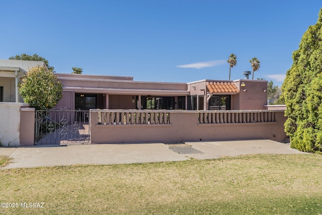 view of front of home with stucco siding, a front lawn, a tile roof, a fenced front yard, and a patio