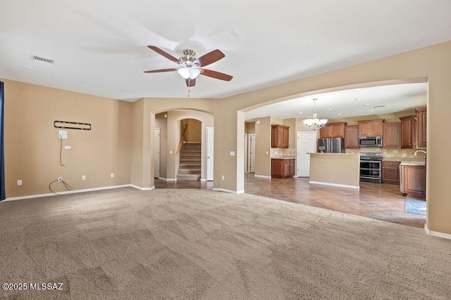 unfurnished living room with stairway, visible vents, arched walkways, carpet flooring, and ceiling fan with notable chandelier