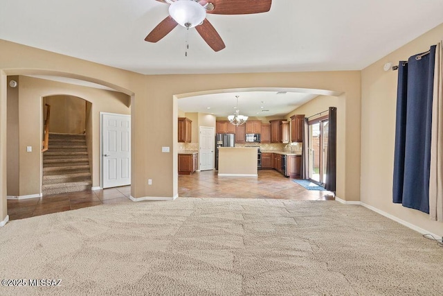 unfurnished living room featuring light carpet, light tile patterned floors, ceiling fan with notable chandelier, and arched walkways