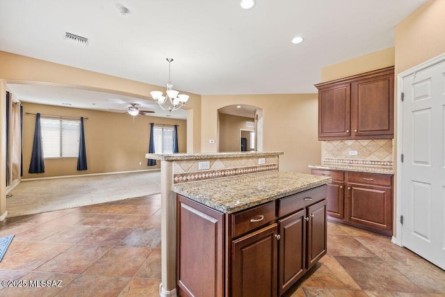 kitchen featuring visible vents, a kitchen island, tasteful backsplash, open floor plan, and arched walkways